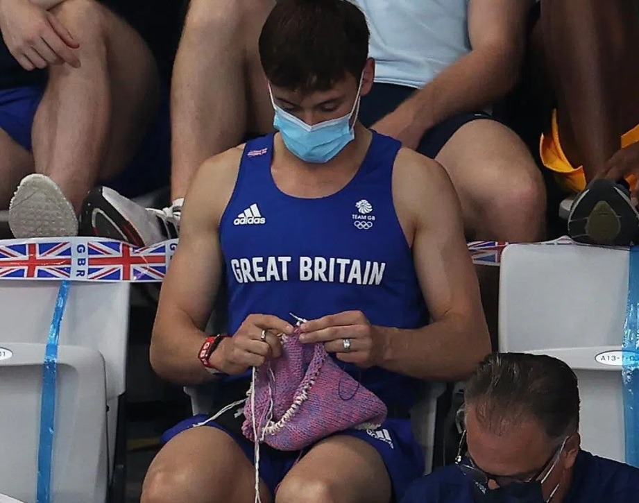 Tokyo Olympics Champion Tom Daley Knitting Pink Pouch During Women’s Springboard Diving Final Goes Viral. Tom Daley knitted pink pouch on Live TV.