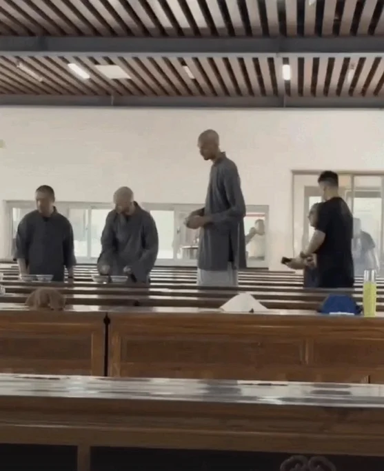 Bald Victor Wembanyama towering over everyone inside a cafeteria at a Shaolin Temple in Kung Fu gear