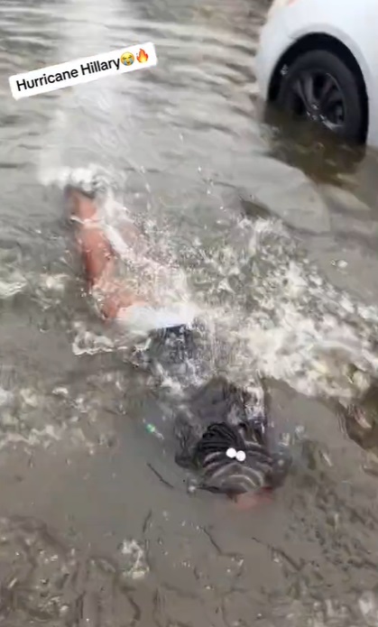 black woman swimming through Hurricane Hilary flood water while celebrating